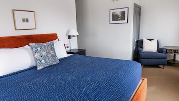 A neatly arranged hotel room with a large bed, a chair, a small table, and two framed pictures on the walls.