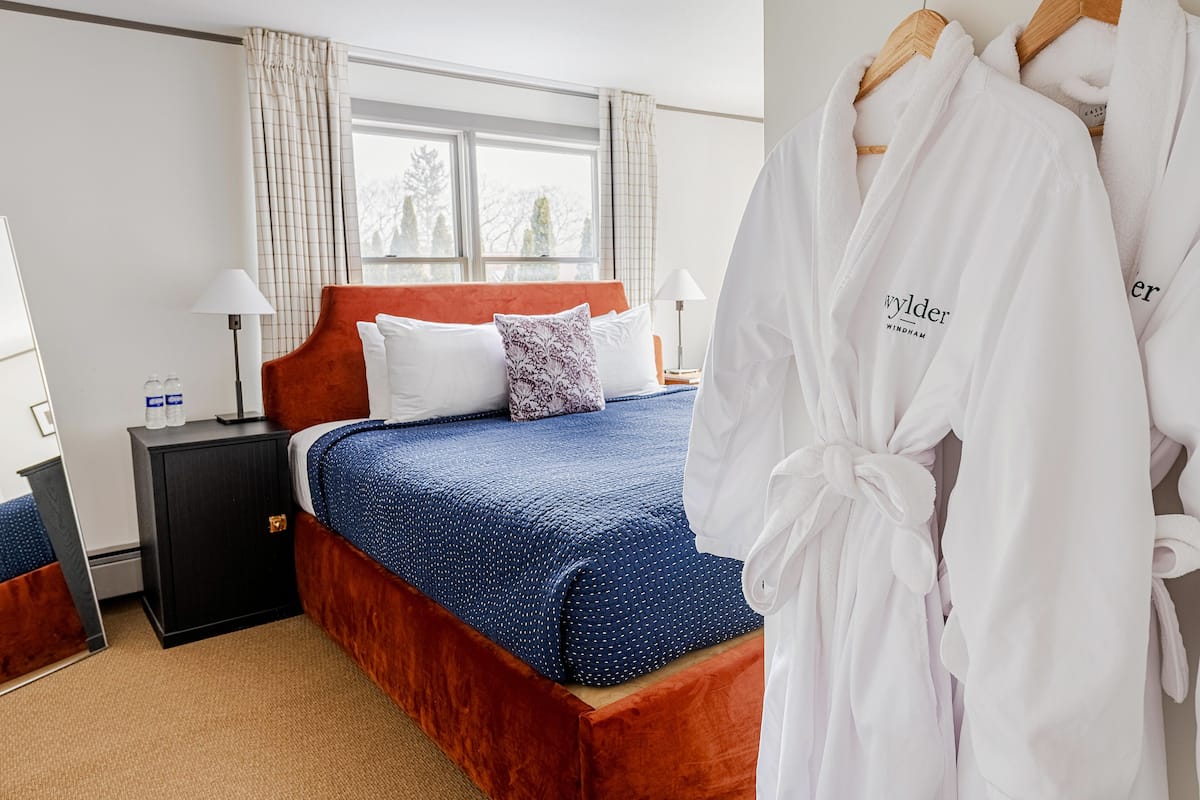 A hotel room with a bed, a nightstand, a lamp, and a window with curtains.