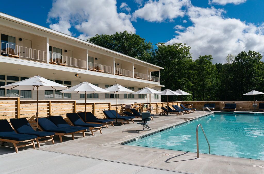 Un espace aménagé au bord de la piscine, avec des chaises longues et des parasols, une piscine, et un bâtiment doté de balcons.