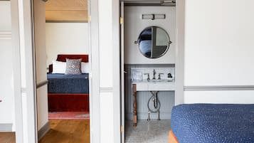 Una habitación con cama, un baño con lavabo y espejo, y una puerta que da a otra estancia.