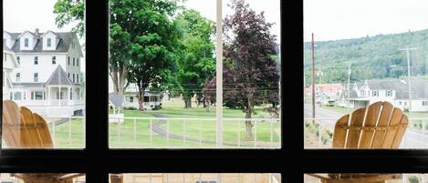 A view from a window with wooden chairs, a lawn, and houses in the background.