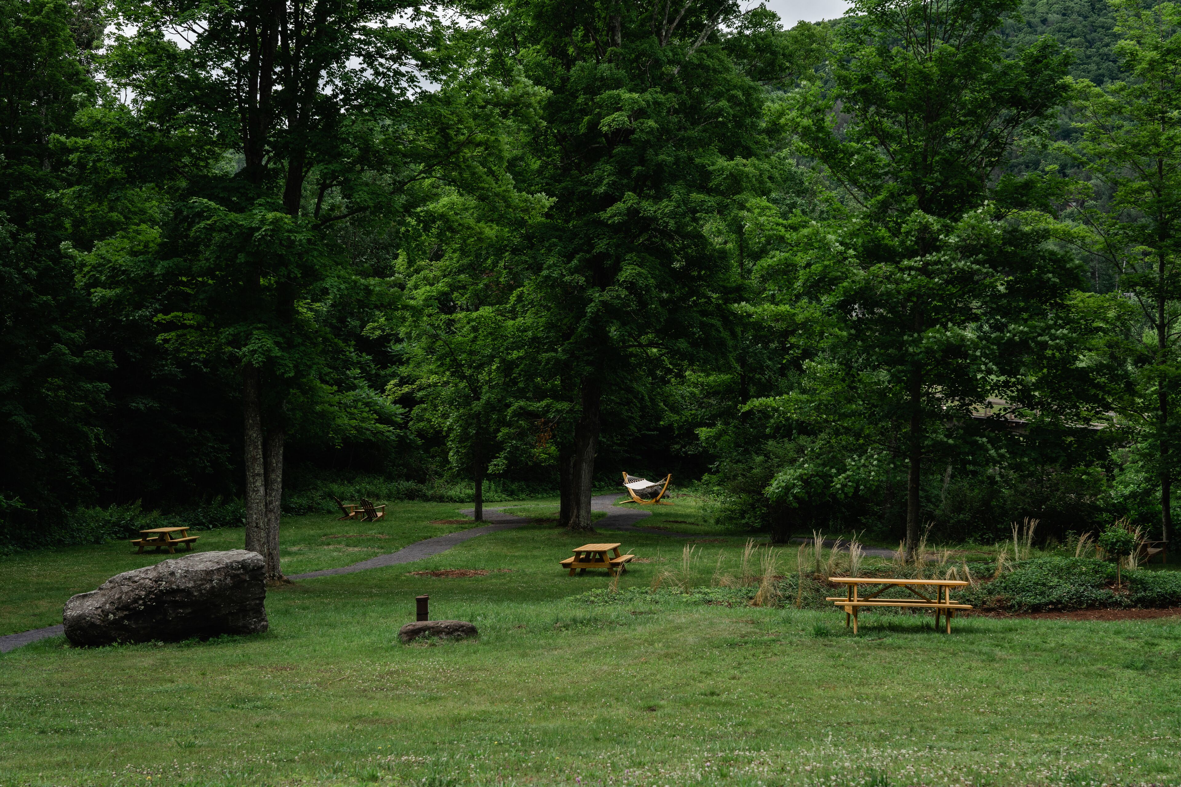 Un parque con mesas de picnic, una hamaca y una gran roca.