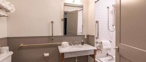 Ein Badezimmer mit Toilette, Waschbecken und Badewanne. Haltegriffe sind in der Nähe der Toilette und des Waschbeckens angebracht.