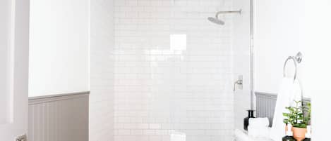 A modern bathroom with white subway tiles, a glass shower enclosure, a white sink, and a mirror.