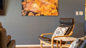 Ein Zimmer mit einer dunkelgrauen Wand, einem Holzstuhl mit gemustertem Sitzkissen und einem großen Landschaftsbild.