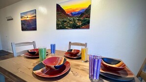 Ein Esstisch mit bunten Tellern und Gläsern, zwei Stühle und zwei Bilder an der Wand.