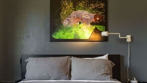 Ein Schlafzimmer mit Bett, Kissen, einem Nachttisch, einer Lampe und einem Bild von einem Kanu-Fahrer auf einem Fluss.