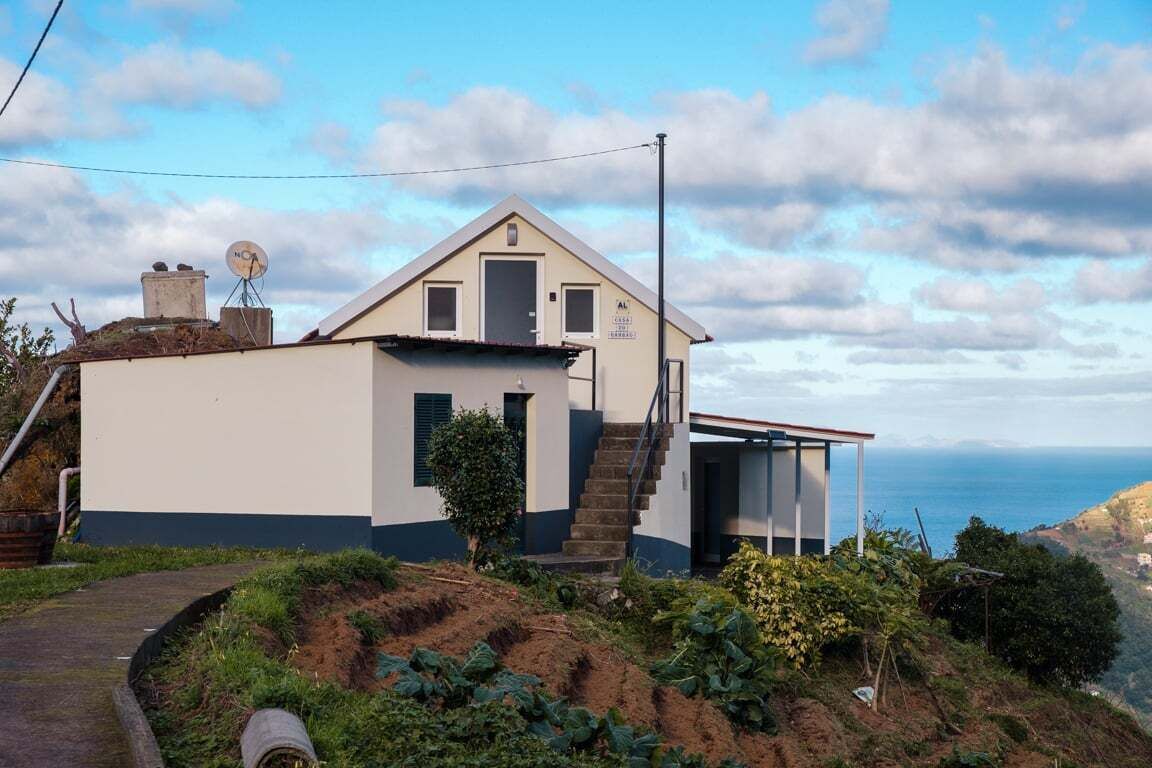 A two-story house with a small balcony, a satellite dish, and a view of the sea.