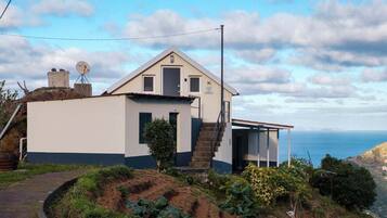 A two-story house with a small balcony, a satellite dish, and a view of the sea.