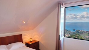 Ein Schlafzimmer mit großem Fenster und Blick auf die Küste, einem Holzkopfteil und einer Nachttischlampe.