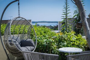 A wicker hanging chair with a cushion, a small round table, and lush greenery.