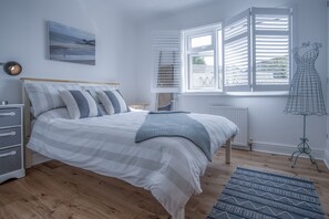 A bedroom with a bed, a dresser, a radiator, a window with blinds, a wall-mounted artwork, and a mannequin.