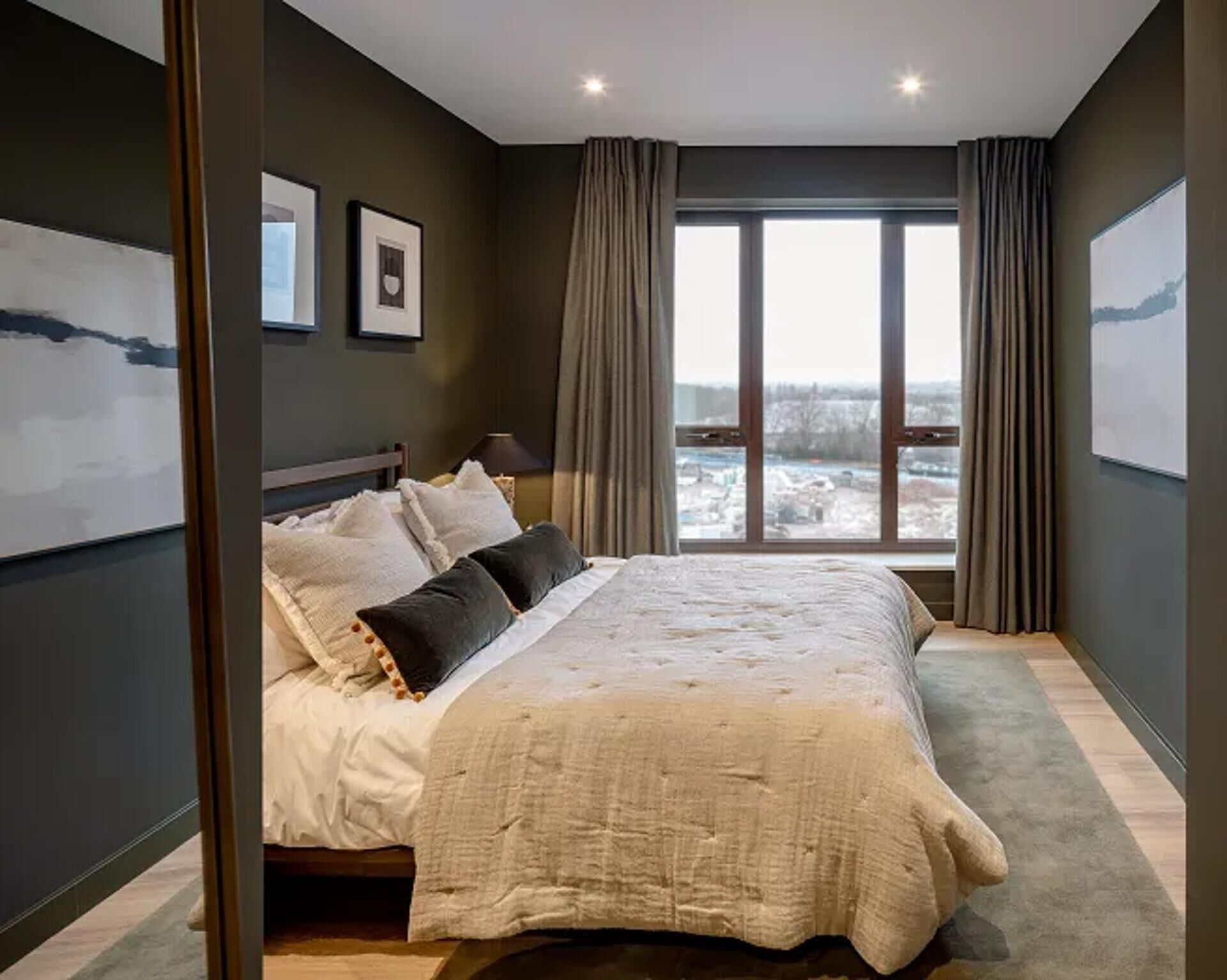 A modern bedroom with a large bed, a view of a snowy landscape through a large window, and a framed picture on the wall.
