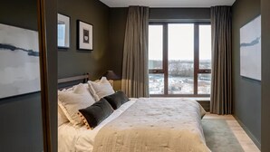 A modern bedroom with a large bed, a view of a snowy landscape through a large window, and a framed picture on the wall. - Luxurious 2bed Apartment in Greenford Quays (Greenford)