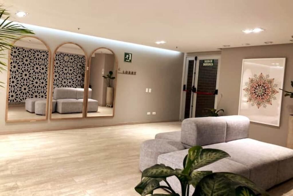 En moderne hotellobby med en grå sofa, en dekorativ væg med geometrisk mønster og et stort spejl, der reflekterer rummet.