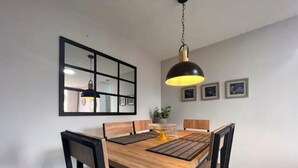 Un coin repas avec une table en bois, des chaises noires, une suspension, un miroir et des tableaux encadrés accrochés au mur.