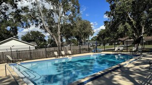 A rectangular swimming pool with a tiled edge, surrounded by a fence, and shaded by trees. - 3/2 Home Minutes To All Theme Parks (Orlando)