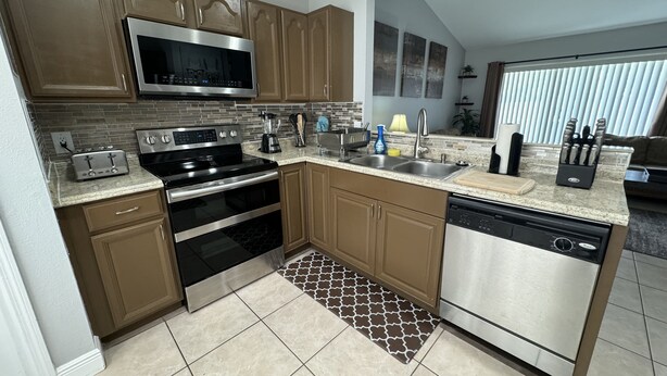 A modern kitchen with stainless steel appliances, wooden cabinets, and a tiled floor. - 3/2 Home Minutes To All Theme Parks (Orlando)