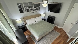 A bedroom with a bed, bedside tables, a lamp, a TV mounted on the wall, and a patterned rug. - 3/2 Home Minutes To All Theme Parks (Orlando)