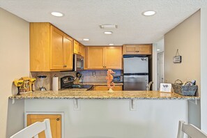 A kitchen with wooden cabinets, a stainless steel refrigerator, and a granite countertop.