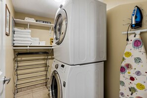 A laundry area with stacked washing machines, a drying rack, and a shelf with folded towels.