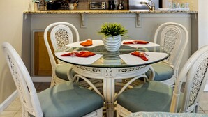 A dining area with a glass table surrounded by wicker chairs with cushioned seats. A potted plant is on the table, and there are napkins and a glass on each chair. - Beachside Charm! Just A Short Stroll To Miles Of Pristine Beach. (St. Augustine)