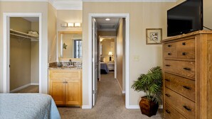A hotel room with a bed, a wooden dresser, a television, and a bathroom with a sink and mirror. - Beachside Charm! Just A Short Stroll To Miles Of Pristine Beach. (St. Augustine)
