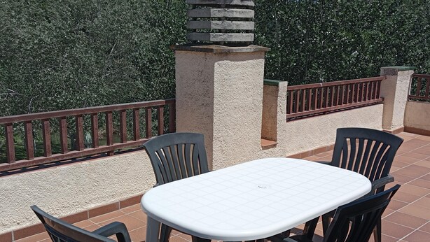 Une terrasse extérieure avec une table blanche et quatre chaises, entourée d’un sol carrelé et d’une rambarde en métal.