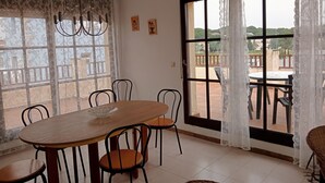 Ein Essbereich mit einem Holztisch und Stühlen, großen Fenstern mit Spitzenvorhängen und Blick auf einen Balkon.
