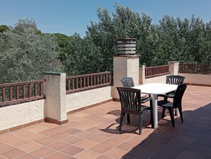 Een terras buiten, met een ronde tafel en vier stoelen, omgeven door een lage bakstenen muur en een metalen hekwerk.