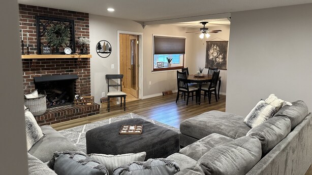 A living room with a fireplace, a dining area with a table and chairs, and a ceiling fan. - Cozy and Comfortable home with easy access to Hwy 60 and Springfield! (Republic)