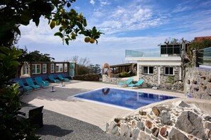 Un área de piscina con una pileta rectangular, paredes de piedra y sillas de descanso azules.