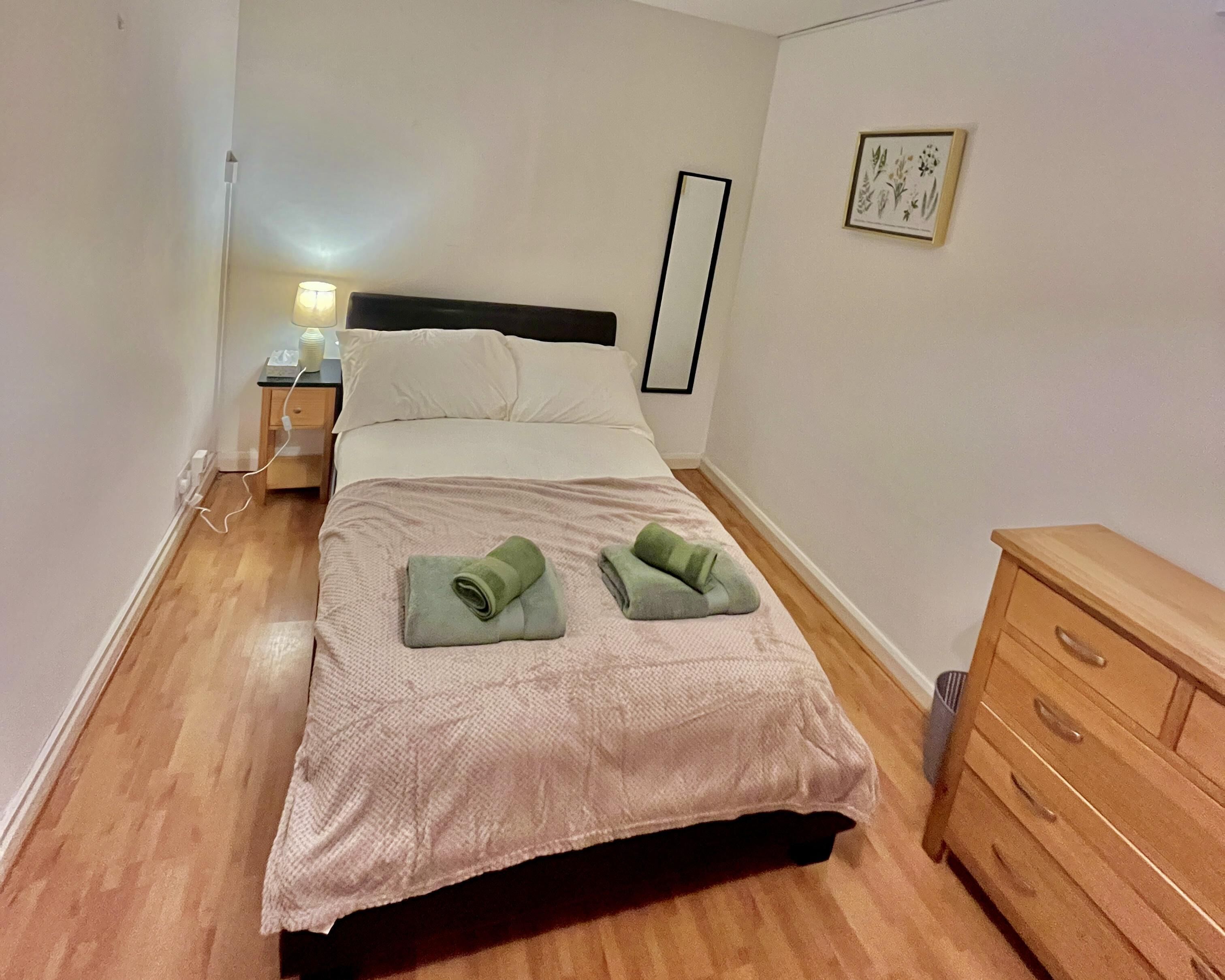 A neatly made bed with a headboard, a bedside table with a lamp, and a dresser.