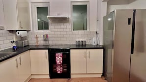 A kitchen with white cabinets, a stainless steel refrigerator, a dishwasher, a toaster, and a window above the sink. - Comfy and Spacious 5-bed House in Cambridge (Cambridge)