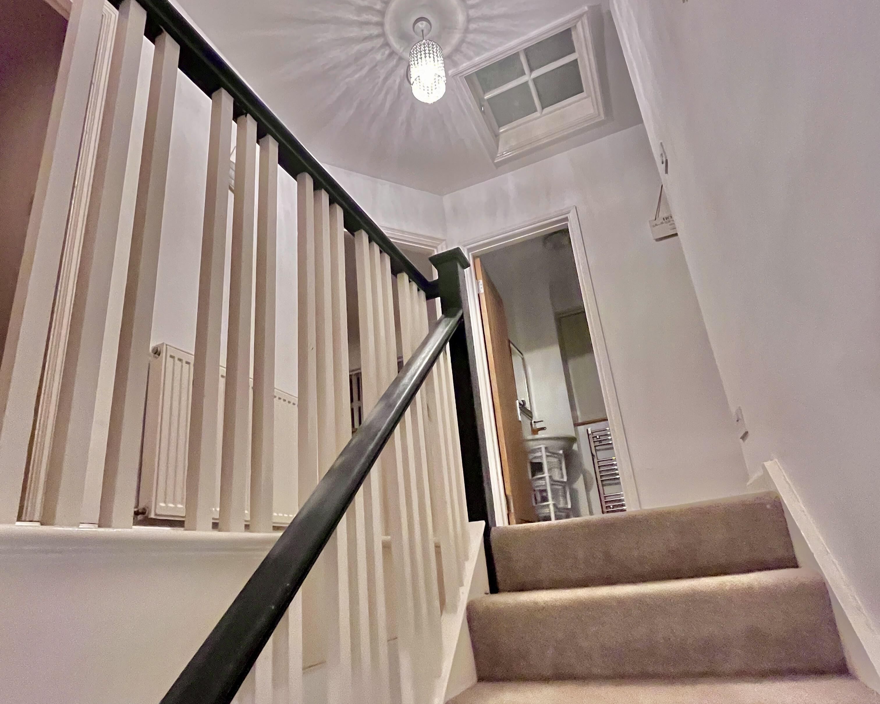 A staircase with white balusters and a black handrail, leading to a room with a ceiling fan and a window.