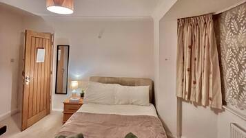 A bedroom with a bed, a nightstand, a mirror, a door, and a window with curtains.