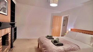 A bedroom with a bed, a wooden headboard, a fireplace, and a door leading to another room. - Comfy and Spacious 5-bed House in Cambridge (Cambridge)