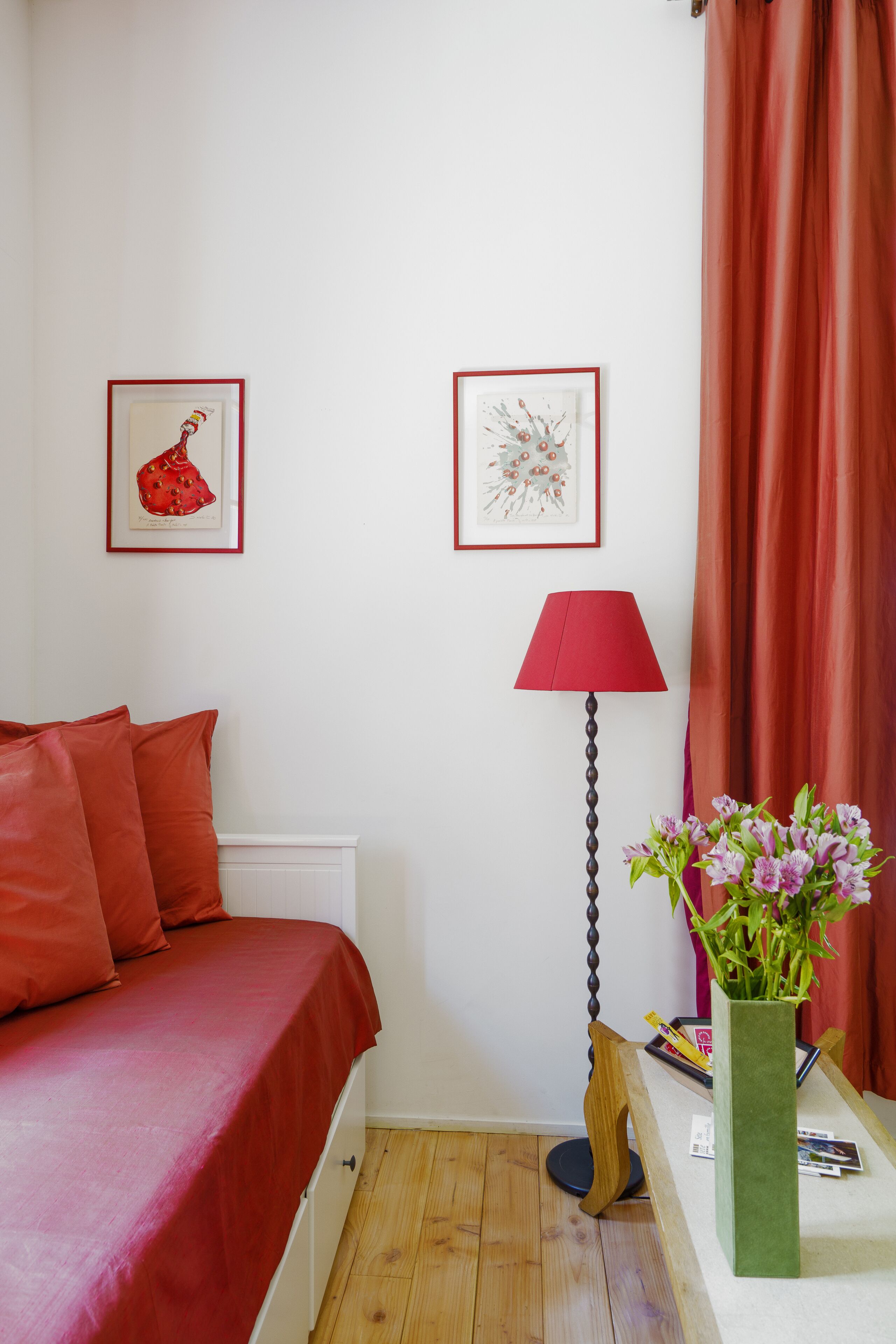 Une chambre avec une couvre-lit rouge, une lampe rouge et deux tableaux encadrés accrochés au mur.