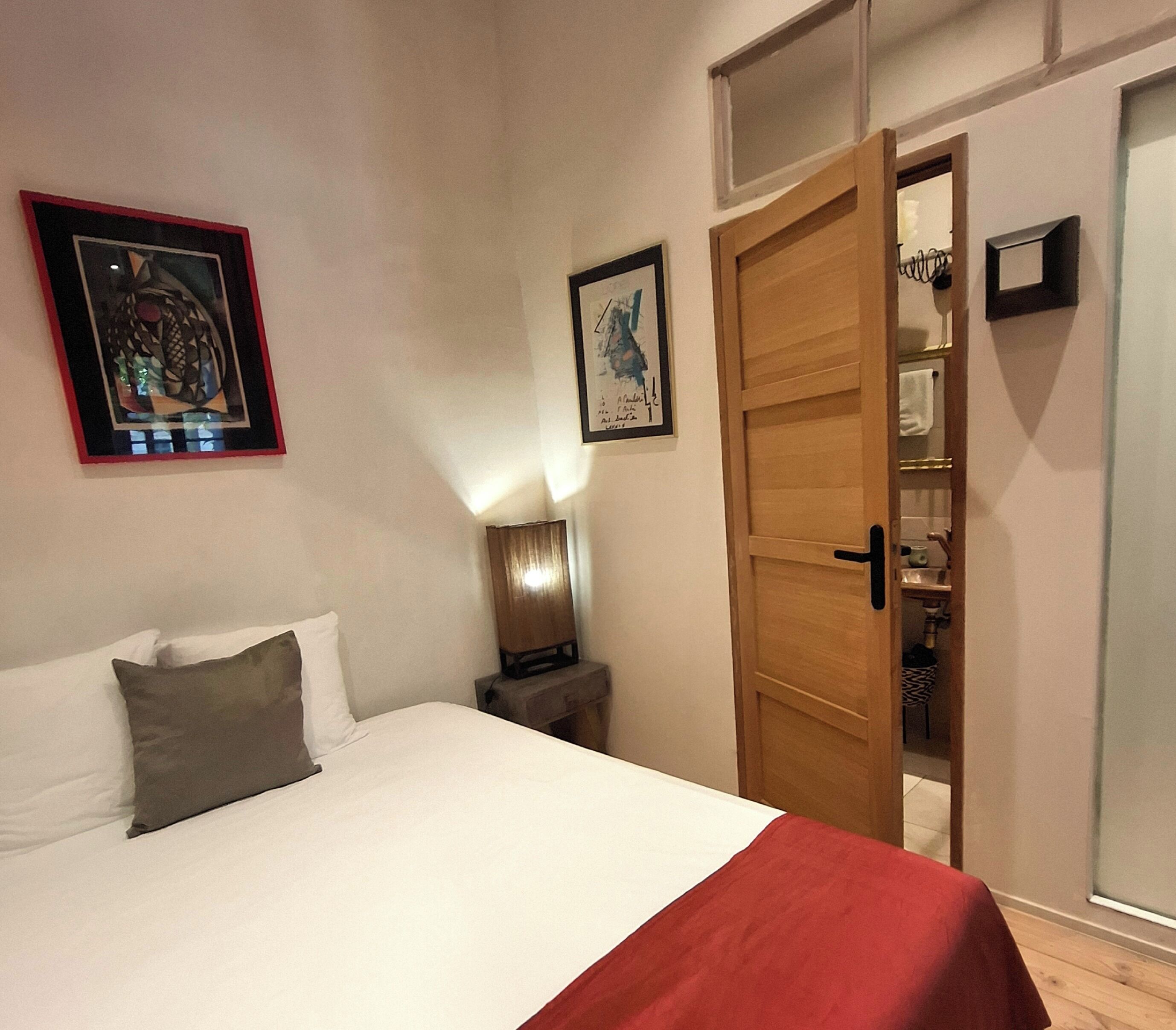 A bedroom with a bed, pillows, a nightstand, a lamp, and a door leading to a closet.