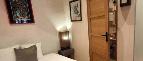 A bedroom with a bed, pillows, a nightstand, a lamp, and a door leading to a closet.