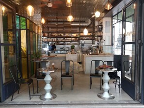 Een café met ronde tafels, stoelen en een balie waar iemand eten bereidt.