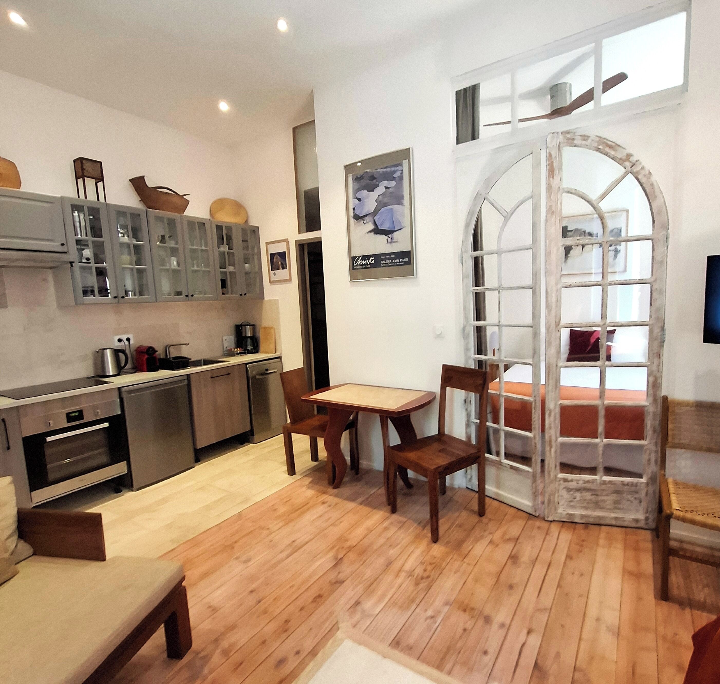 Una cocina compacta con electrodomésticos modernos, un comedor con una mesa y sillas de madera, y un amplio ventanal arqueado.