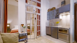 Un espacio habitable compacto con kitchenette, sofá, comedor y un dormitorio visible a través de una puerta abierta.