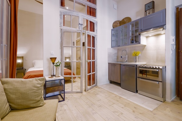A compact living space with a kitchenette, a sofa, a dining area, and a bedroom visible through an open door.