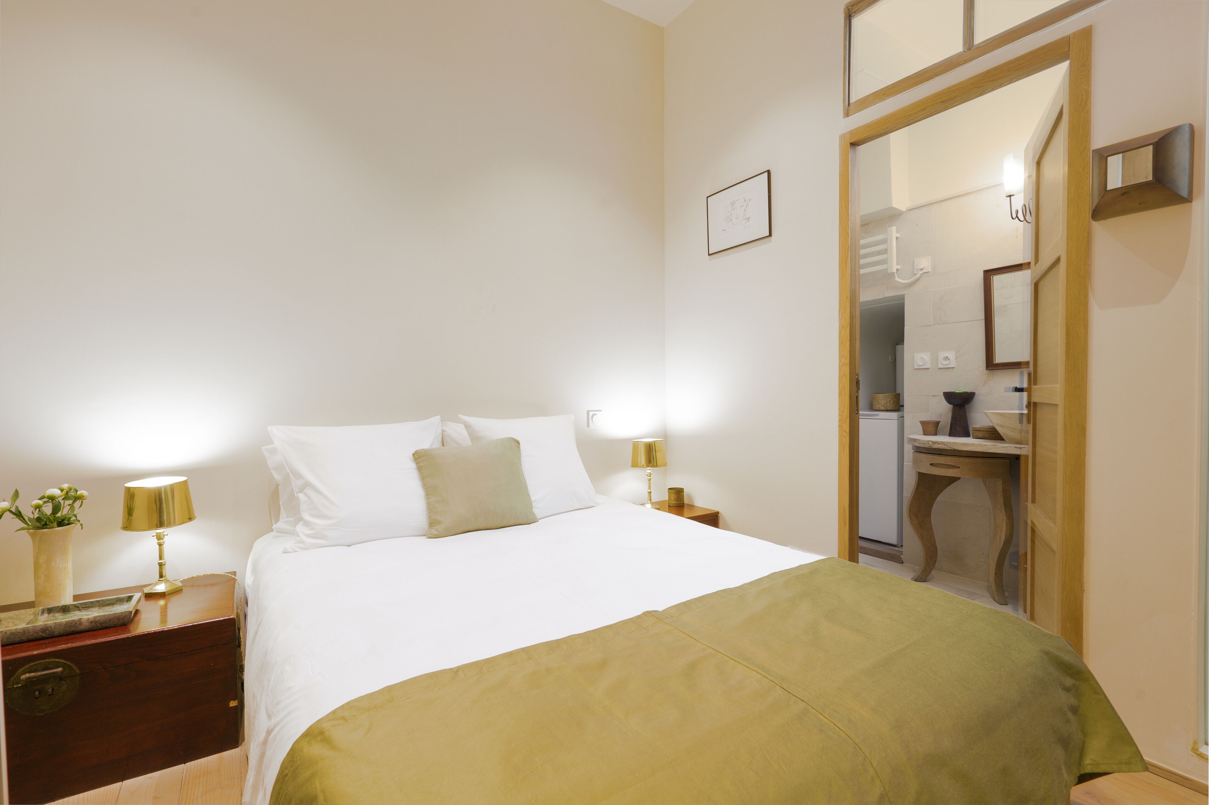 A hotel room with a bed, bedside lamps, a nightstand, a small table, and a mirror.