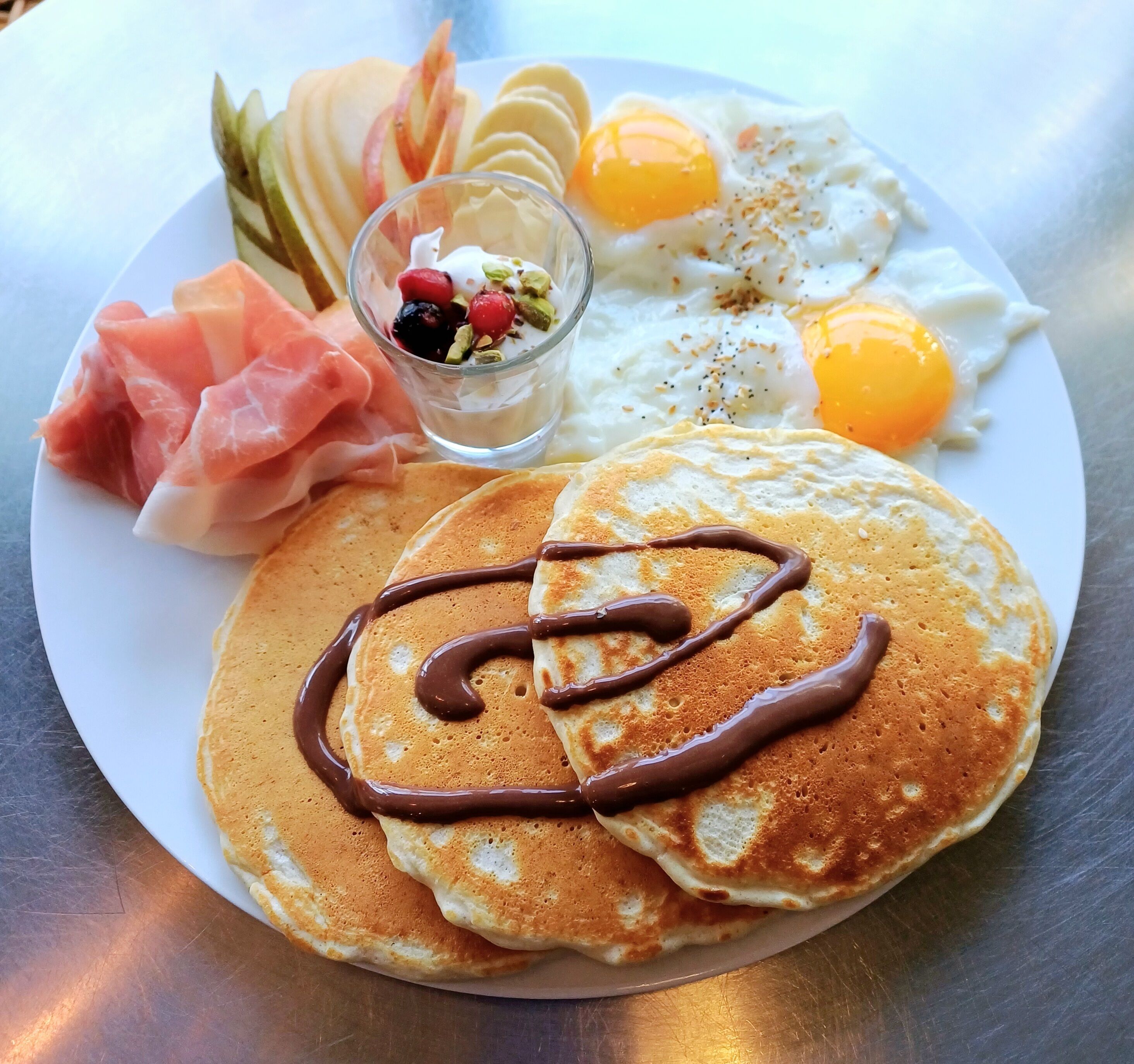 A plate with pancakes, eggs, smoked salmon, and a small dessert.