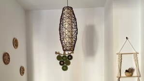 Un coin repas avec une table en bois et quatre chaises, un luminaire suspendu en macramé et des assiettes décoratives fixées au mur.
