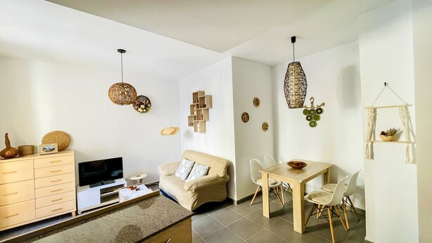 Un salon moderne comprenant un canapé, un téléviseur, un meuble en bois et un coin repas avec des chaises et une table.