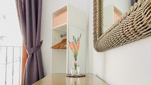 Une pièce avec une table en bois, un miroir, une armoire blanche et une fenêtre avec des rideaux.
