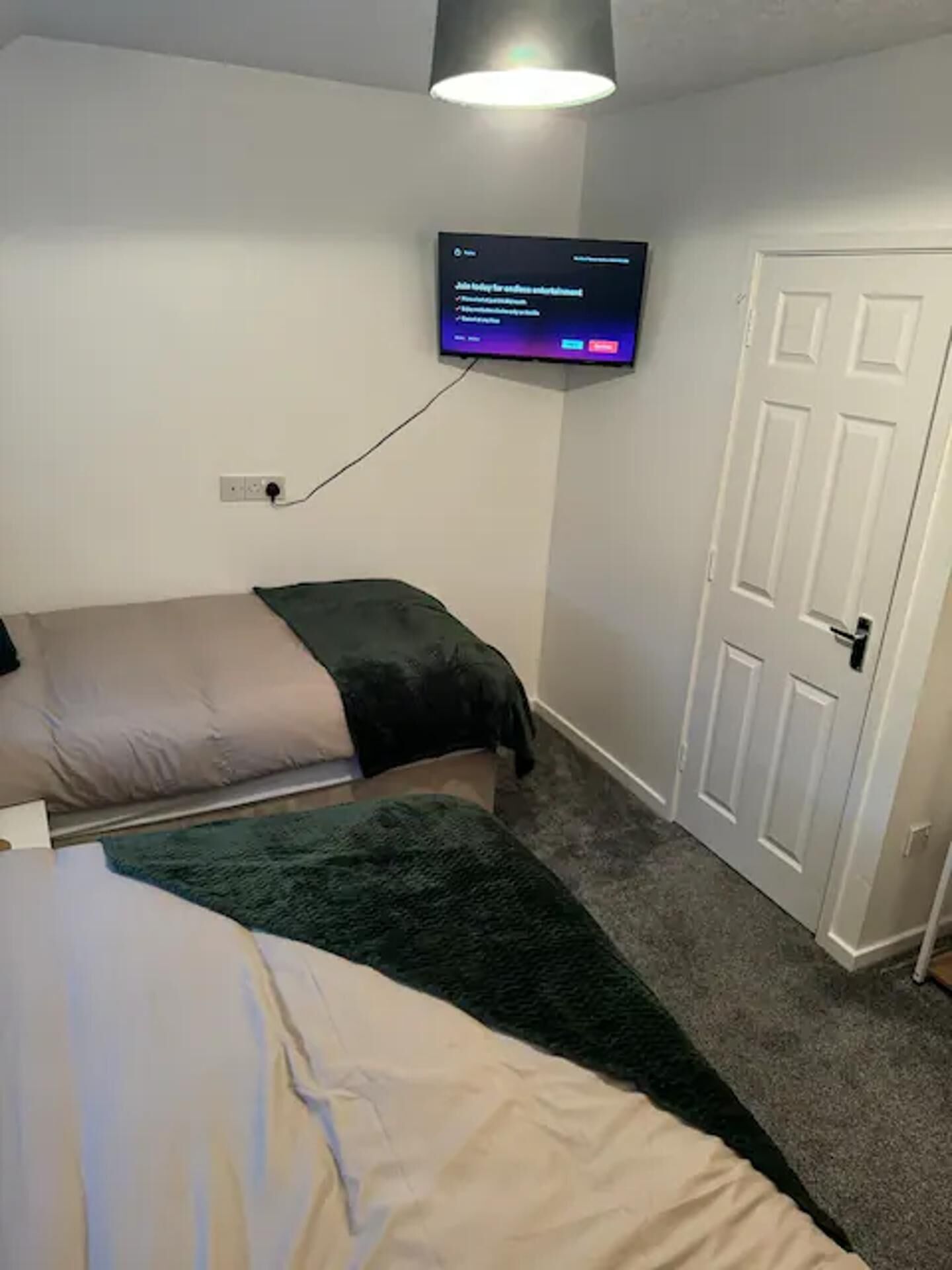 A bedroom with two beds, a television mounted on the wall, and a door.